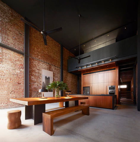 Large kitchen with exposed brick wall and timber and aluminium dining table.