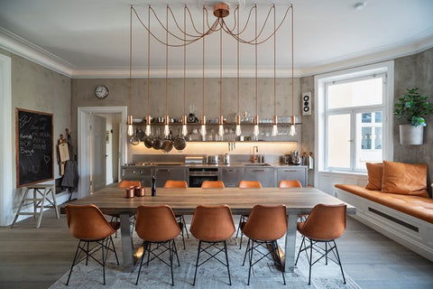 Kitchen with long table, brown chairs and gold pendant exposed light bulbs.