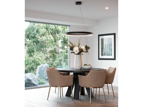 Dining table in front of large window with black hoop-shaped pendant light hanging over dining table