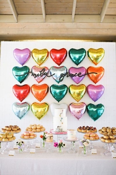 Ballons en formes de cœur disposés sur un mur juste devant une multitude de gâteaux avec bougies