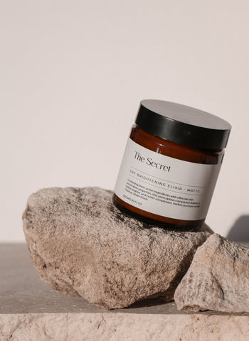 The Secret Skincare's Matte Day Brightening Elixir pictured on a rock - a must have as part of your skincare essentials.