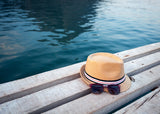 a hat with sunglasses put on a wooden bench near the water