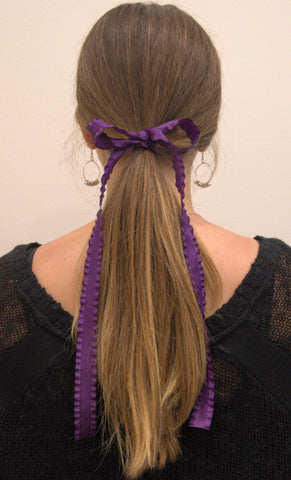 Purple double ruffle ribbon tied in a bow around low ponytail