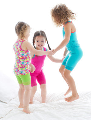 Three girls in tank tops and bike shorts jumping on bed