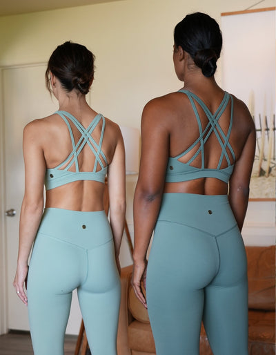 2 models standing side by side wearing the Crimson tavernorlando Leilani Sports bra with their back facing us to show the strap detailing. The leggings are smooth with a vshape seam on the back waistband