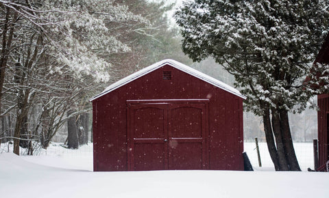 A wooden red garage standing in the heavy snow