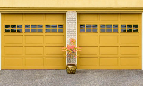 A plant placed between two yellow garage doors
