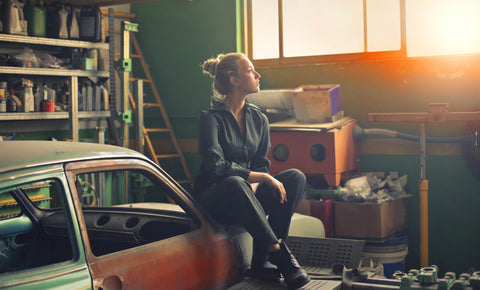 A garage with a car with a woman sitting on top of the car
