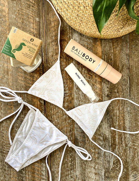 BEIGE FLAT LAY IMAGE WITH BIKINI, BALI BODY TANNING MOUSSE, WHITE BOTTLE OF BLONDI BEACH HAIR TREATMENT, SEAHORSE GREEN & KIND PACKAGING