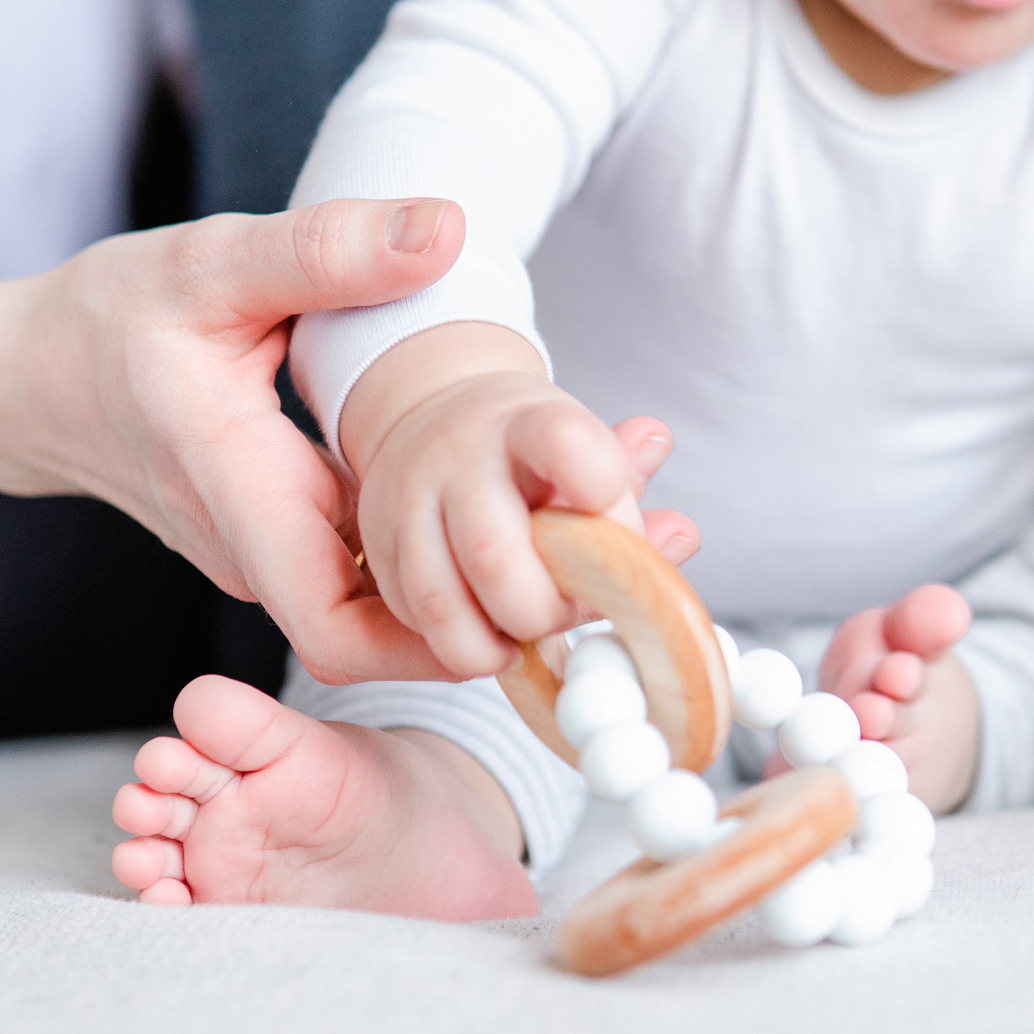 Baby playing with toy while adult hang helps hold up baby's hand. 