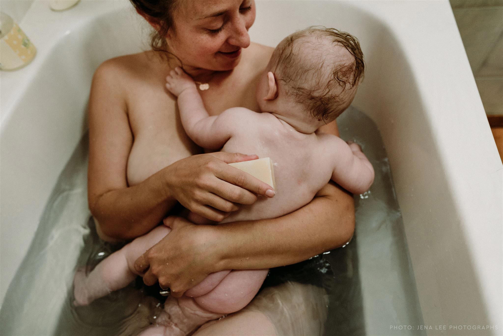 Woman in bathtub with baby lying on her chest. 