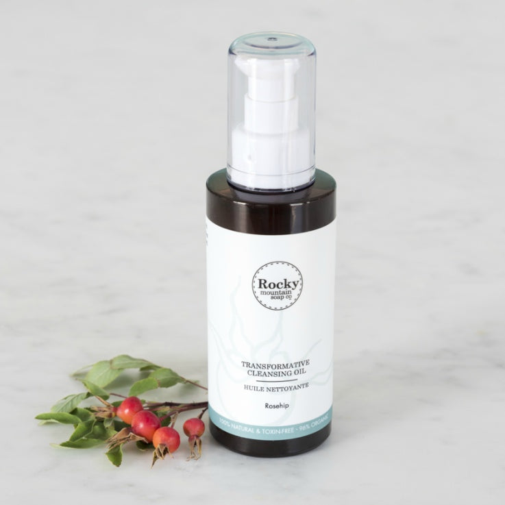Transformative Cleansing Oil bottle next to bright red rosehip buds