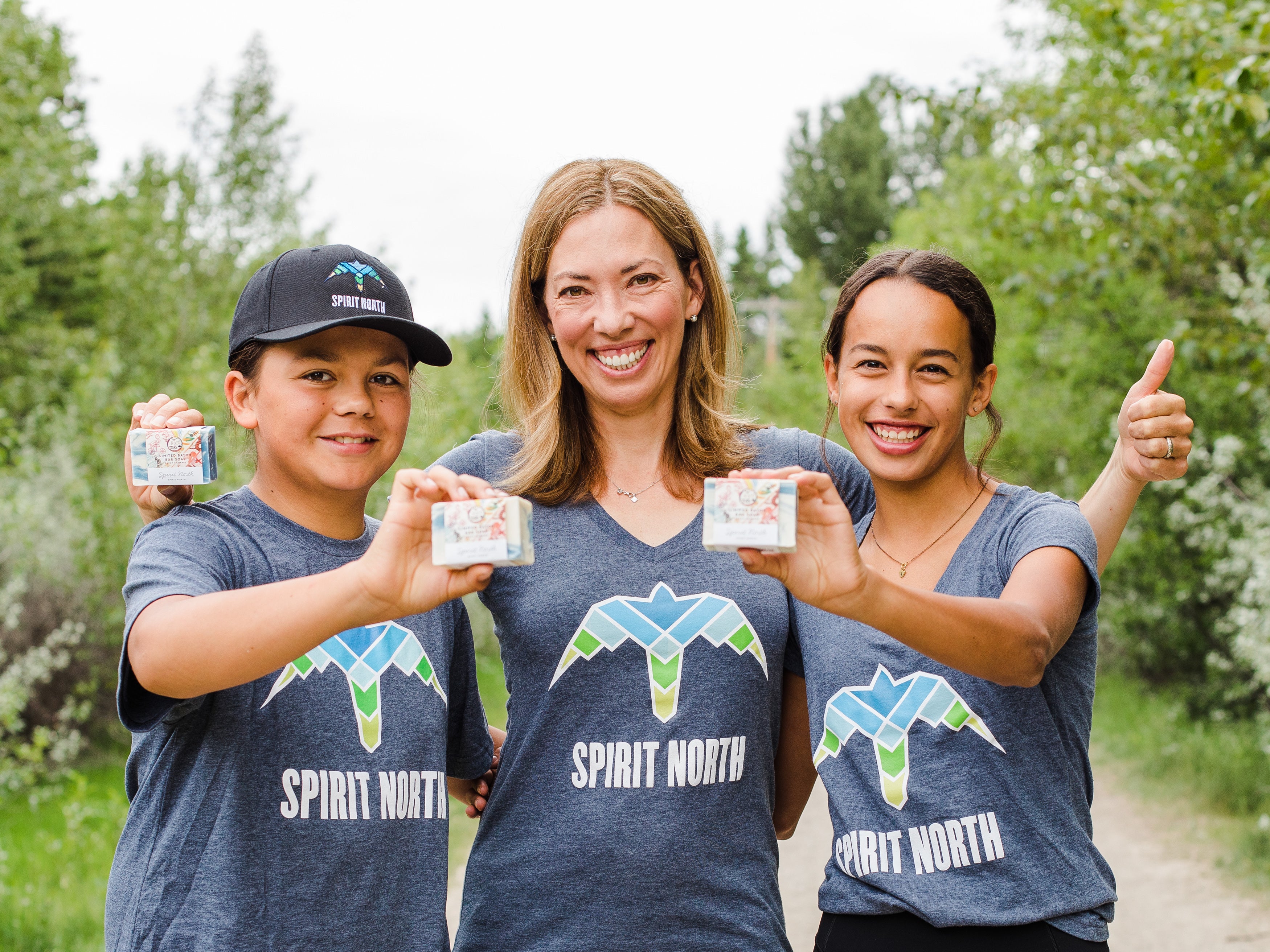 Two children and one adult woman wearing Spirit North t shirts holding natural bar soap. 