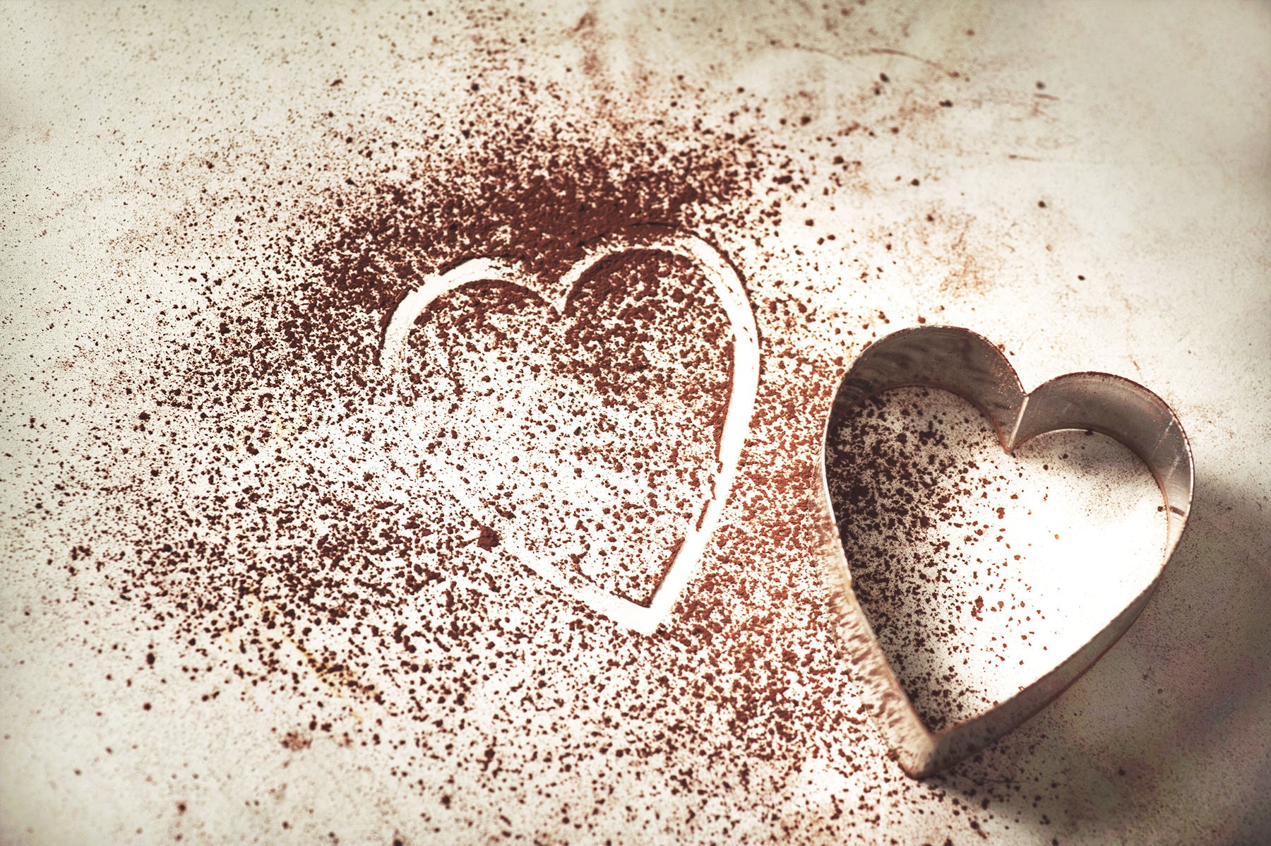 Cocoa powder with a heart shape in the powder from a heart shaped cookie cutter that is next to the cocoa powder. 