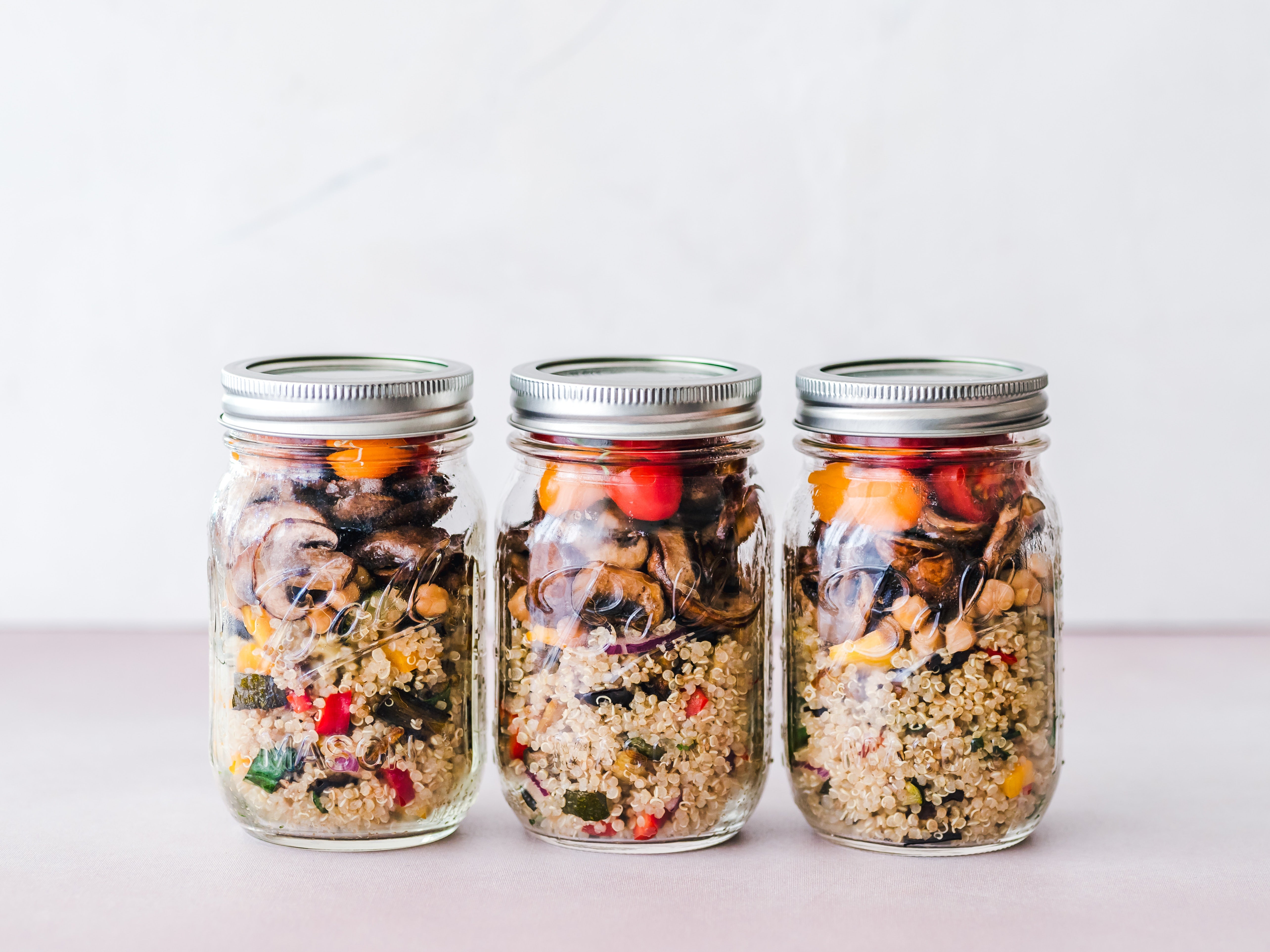 Three mason jars filled with vegetables and grains lined up on a counter. 