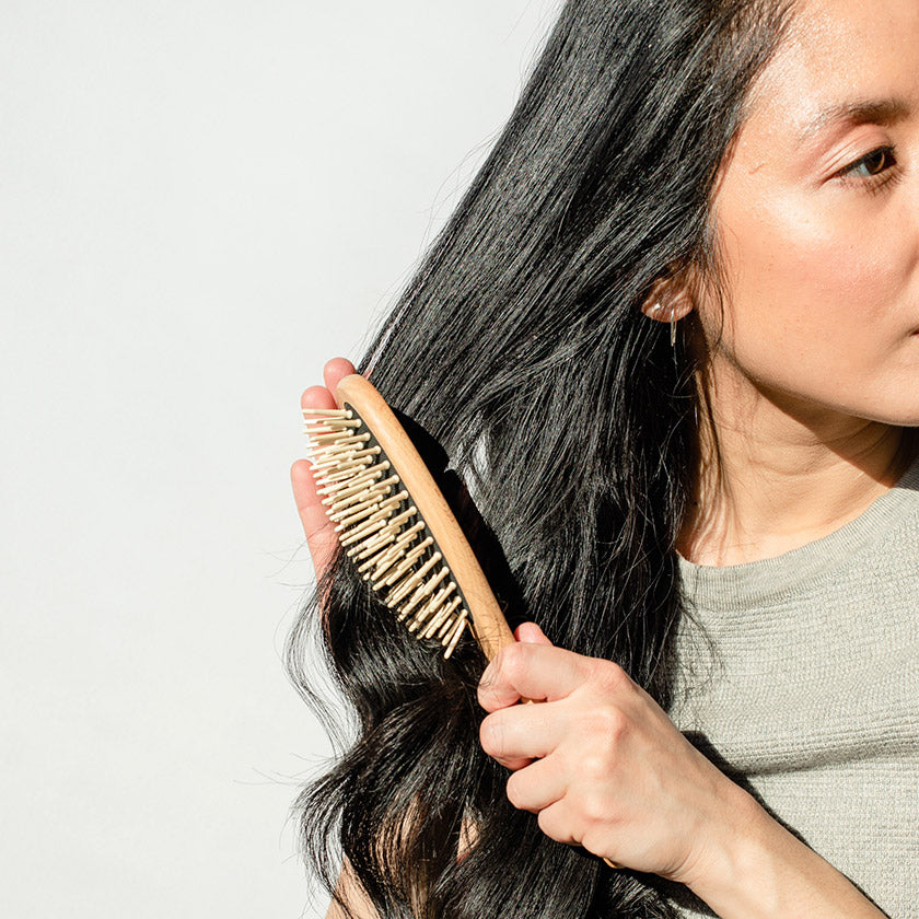 woman using a wooden hair brush to brush her dark brown hair. 