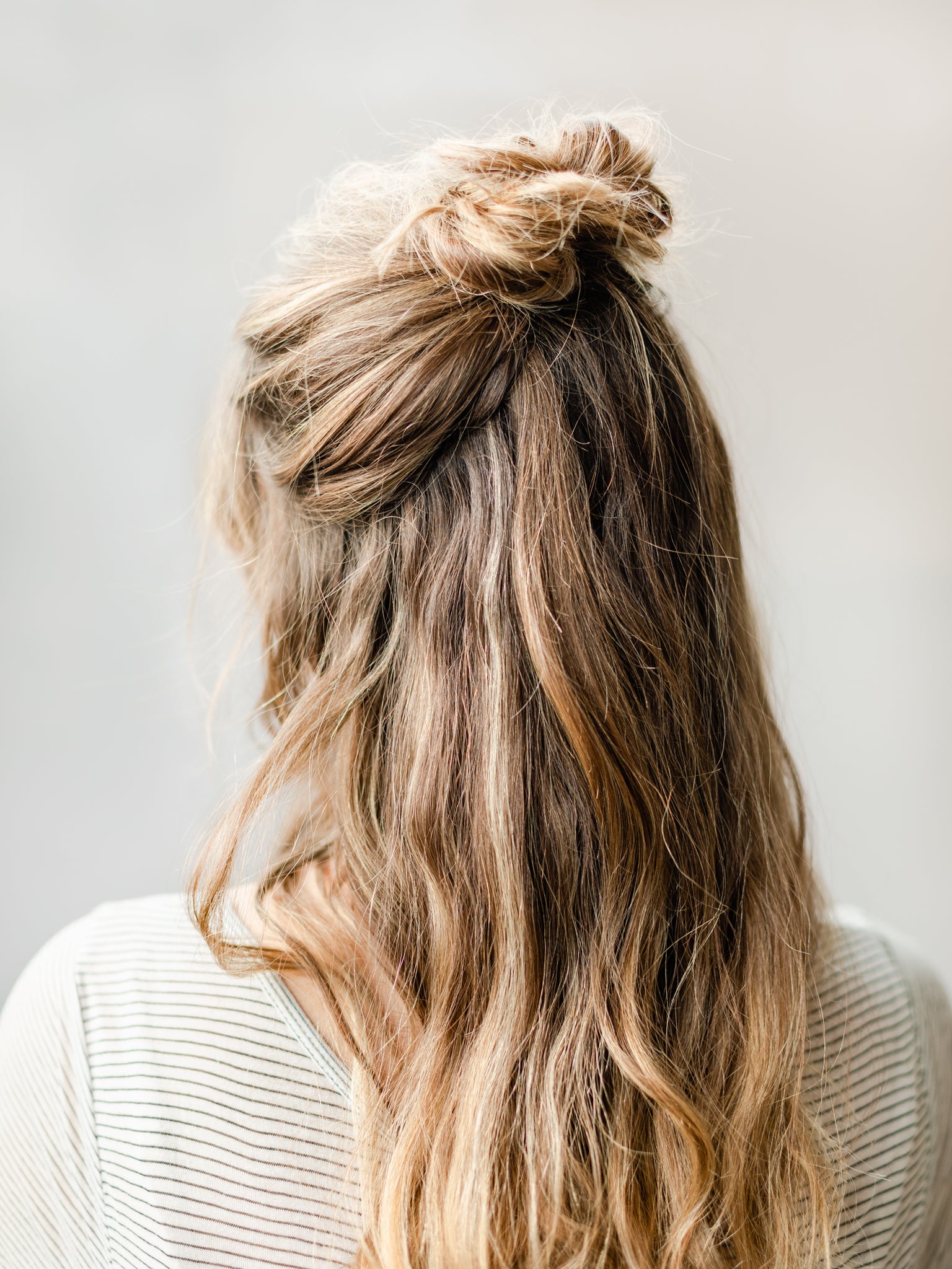 Hair half up in a top knot bun for a sleek easy holiday hairstyle look. 