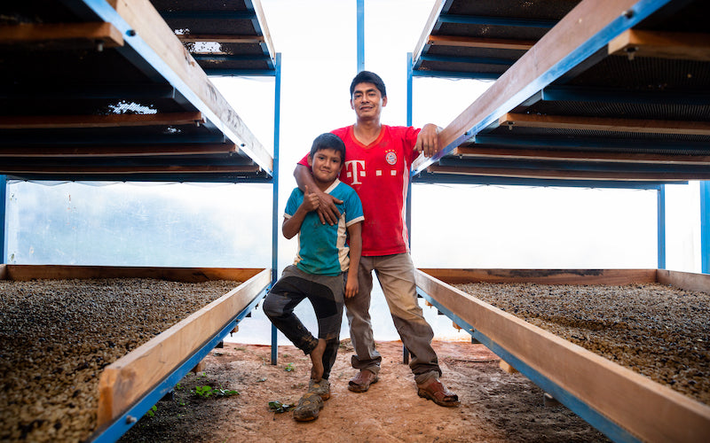 A father and son pose for a photo in a coffee bean drying room.