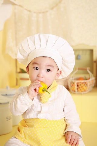 a little boy dressed as a cook, biting into a bright yellow pepper.