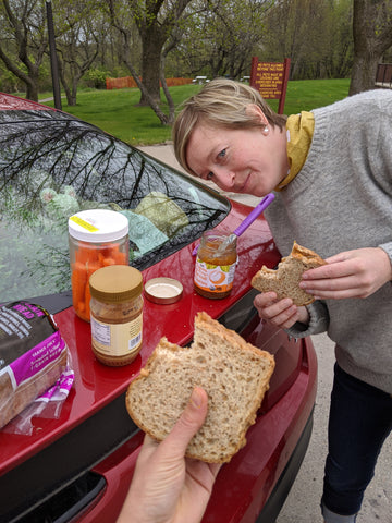 Debbie holding a sandwich and Chelsea eating off the trunk of their car during their cross-country road trip