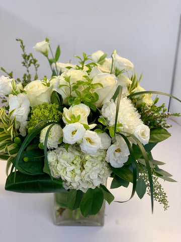 sympathy flower arrangement in a glass vase with white Dahlias Lisianthus hydrangeas commercial mums song of India lily grass roses