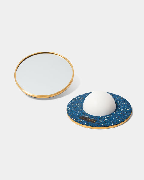 Two round mirrors with brass frame. One of the mirrors is faced downward, with a white half sphere base and speckled blue rubber on its back.