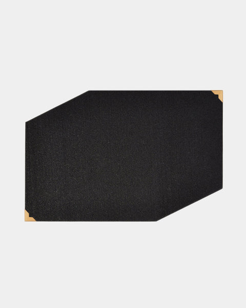 Black rubber geometric placemat with brass corners on white surface.