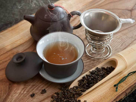 steaming cup of oolong tea next to teapot and other utensils