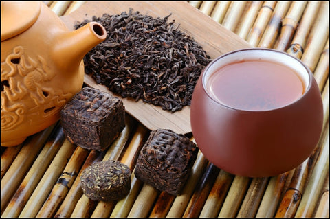a cup of pu-erh tea powder next to a heap of dried oolong tea leaves