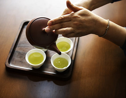 person holding brown teapot pouring tea on white teacups