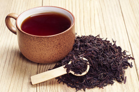 black tea in a brown cup next to a heap of dried black tea leaves