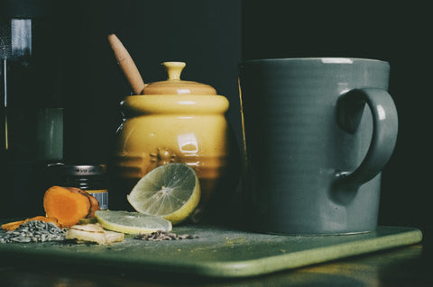 A pot of honey, slices of lemon, and other ingredients next to a mug