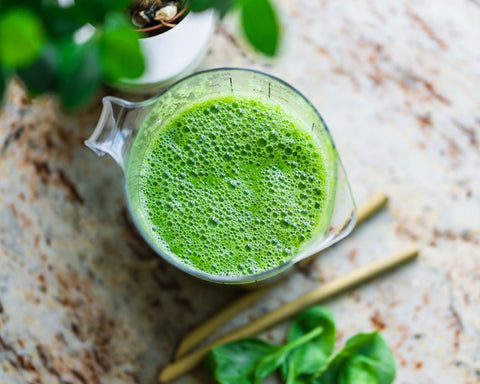 A pitcher full of green smoothie surrounded by straws and leaves