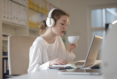 woman wearing headset holding a cup while in front of a white laptop