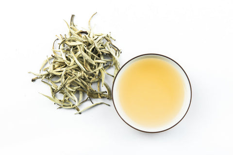 white tea in saucers beside a heap of white tea leaves