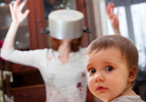 Mom with pot over head stressed out, as baby looks on in wonder.