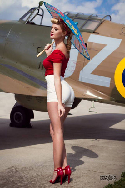 Femme glamour avec des talons hauts rouges et un parasol devant un avion militaire