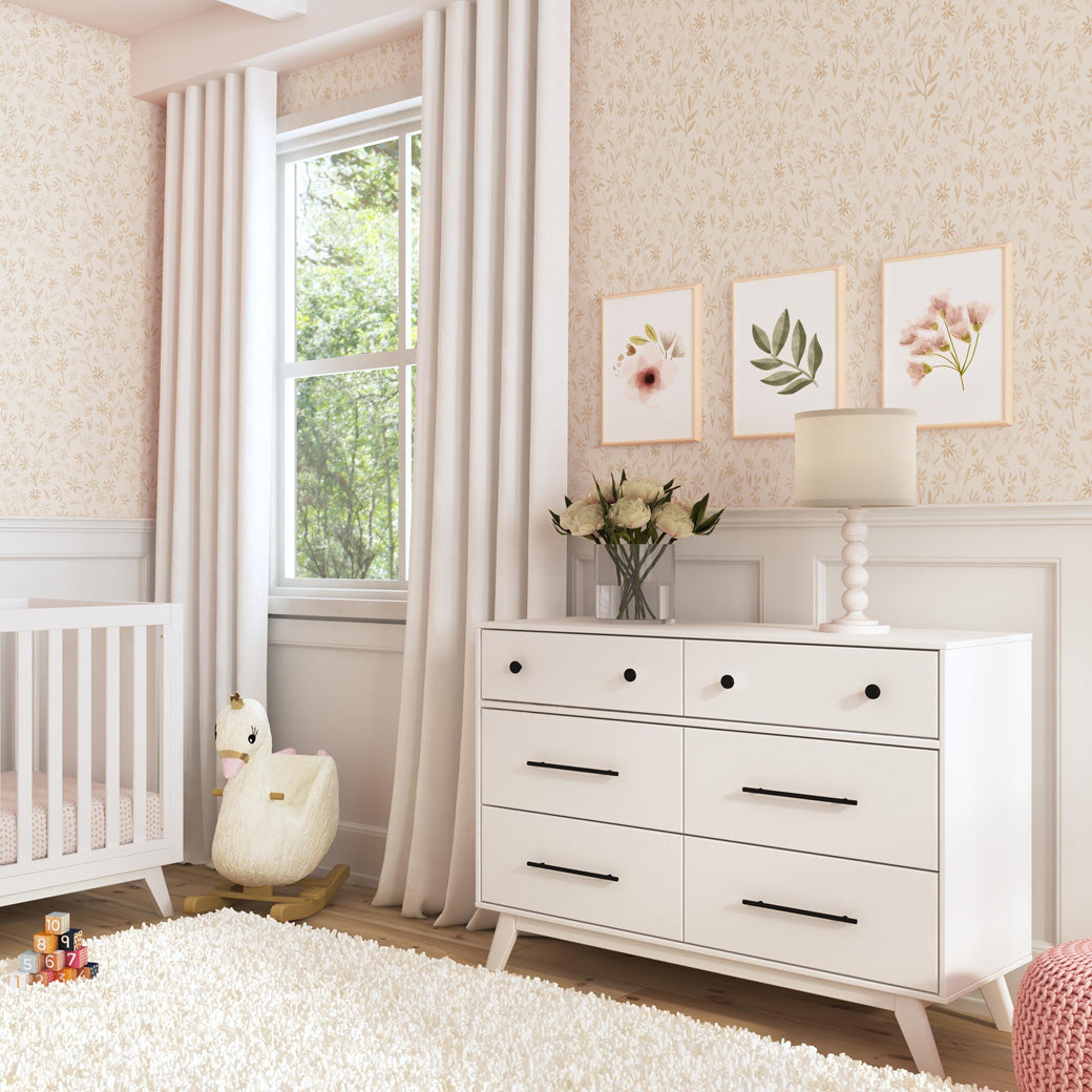 DaVinci Otto 6-Drawer Dresser next to a swan rocker and crib  in -- Color_White