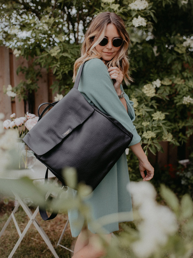 Woman showing off her stylish Storksak diaper bag, a vegan leather black backpack