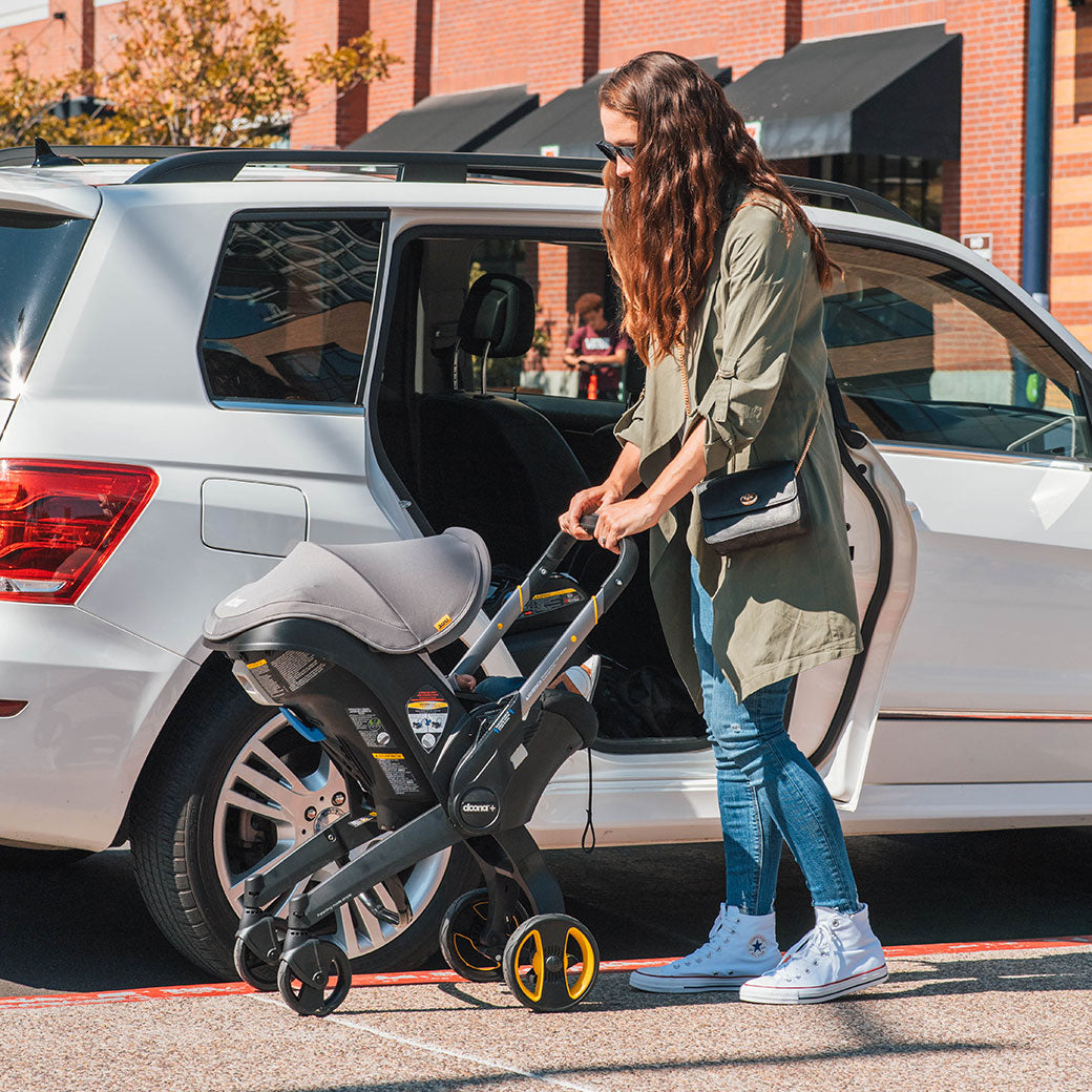 Woman extending the Doona Infant Car Seat and Stroller in Grey Hound so it's a stroller -- Color_Greyhound