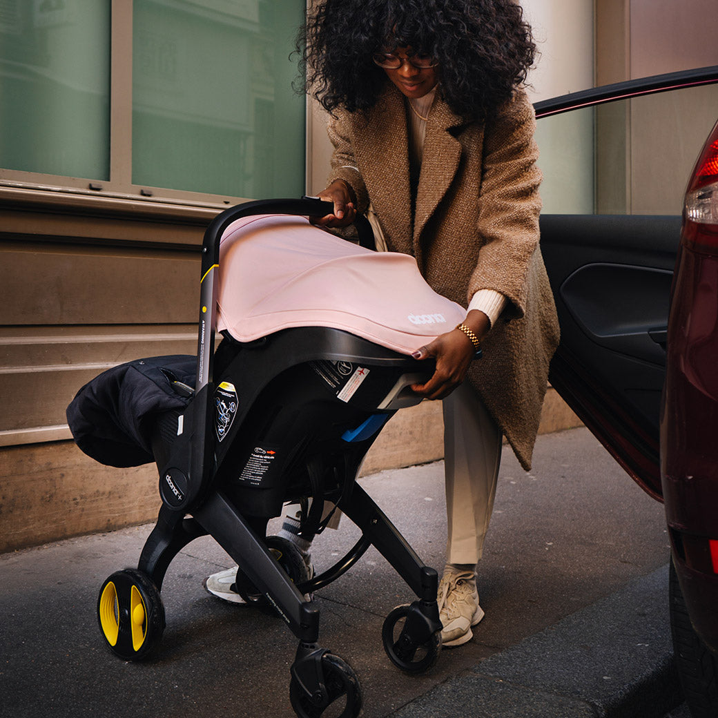 Woman extending the Doona Infant Car Seat and Stroller in Blush Pink after getting the stroller out of the back seat -- Color_Blush Pink