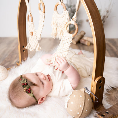 A baby laying and playing with the Finn + Emma Play Gym in -- Color_Natural / Macrame