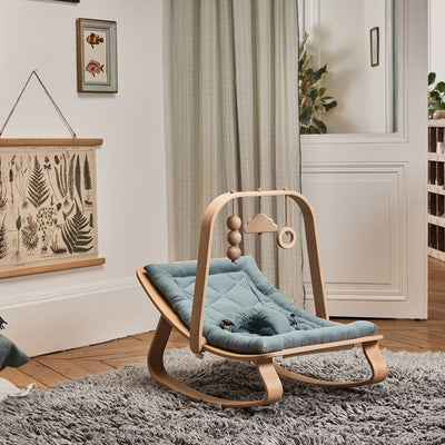 Charlie Crane LEVO Baby Rocker in Orage / Walnut displayed in a baby room with a wooden attachment on it for the baby to play with -- Color_Orage _ Walnut