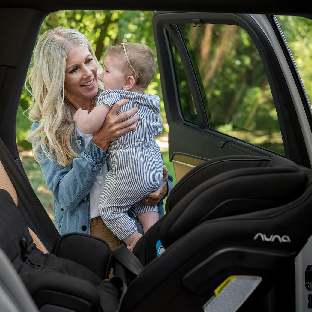 Woman putting baby into Nuna EXEC Car Seat in Color_Ocean in the back of her car — All