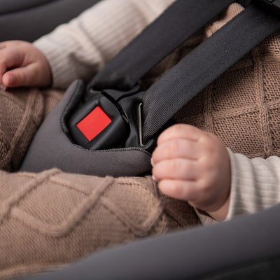Close up of buckle and babies hands in Nuna PIPA lite rx + RELX base in -- Color_Camel