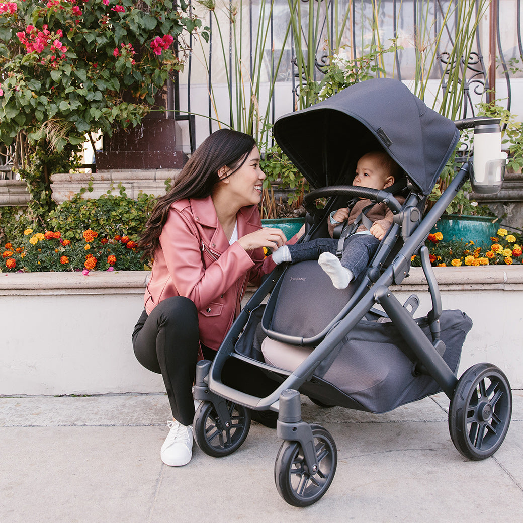 woman kneeling beside the vista v2 stroller in Jake while looking at child in stroller in front of the flower -- Color_Jake