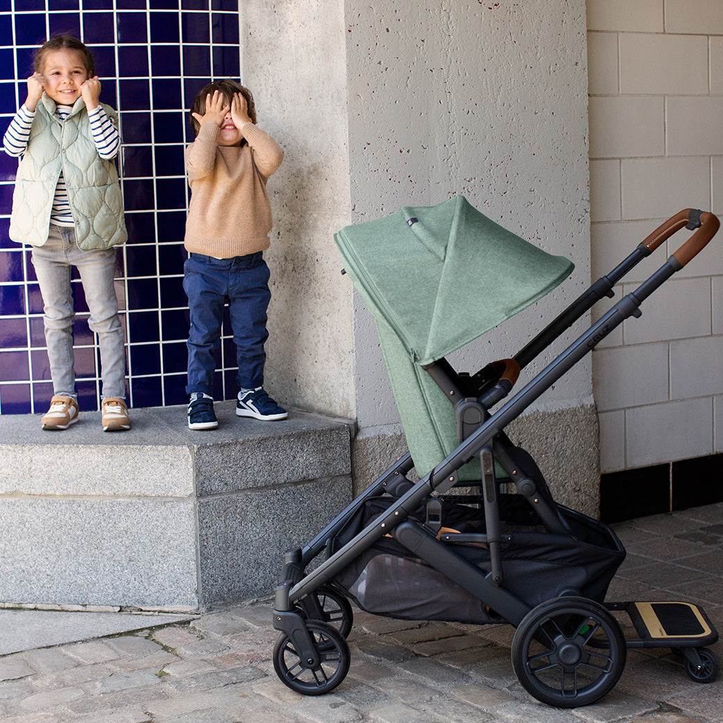 Two toddlers playing and standing next to the UPPAbaby CRUZ V2 Stroller in -- Color_Gwen