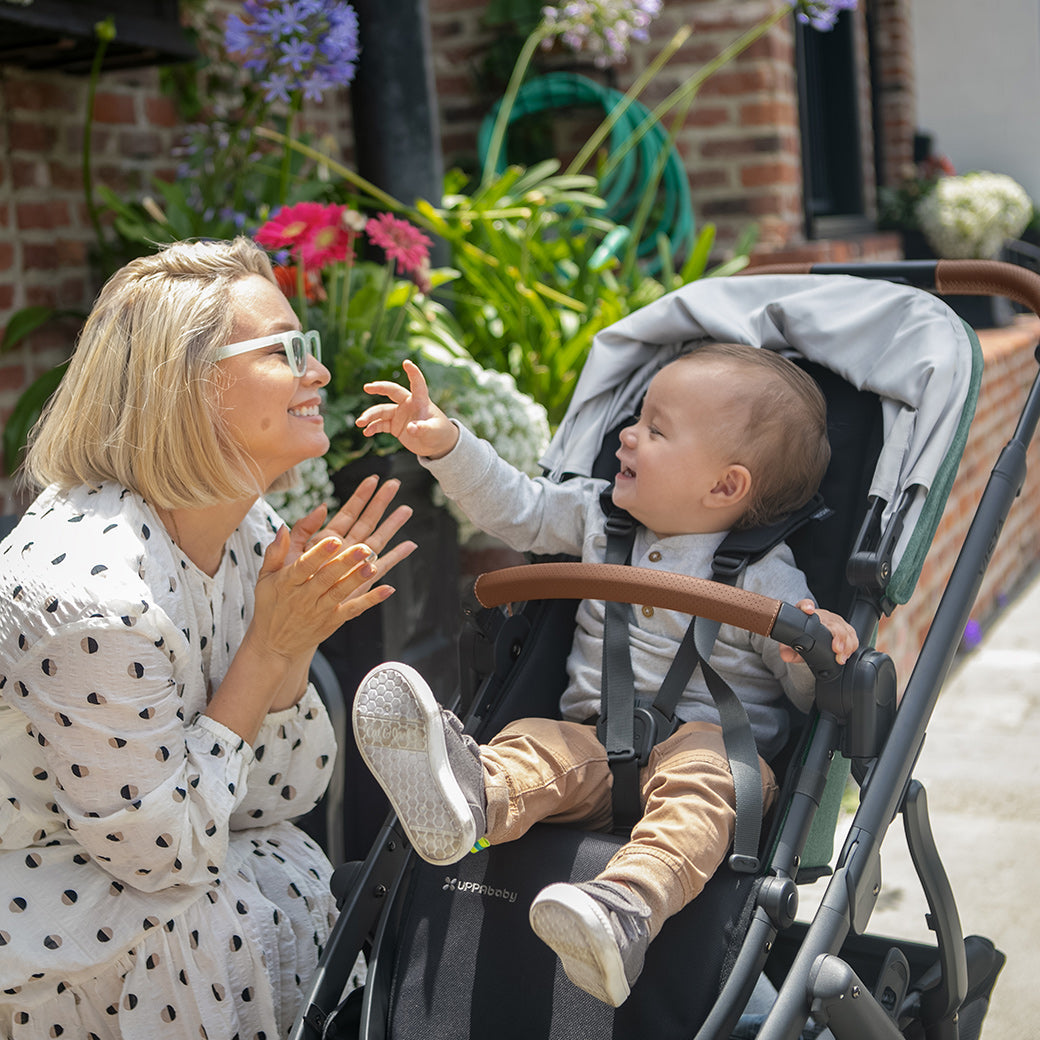 woman kneeling beside the vista v2 stroller in Gwen while looking at child in stroller in front of the flower -- Color_Gwen