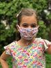 young brown haired girl in a flower shirt wearing her playful pink and patterned mask by gogobags