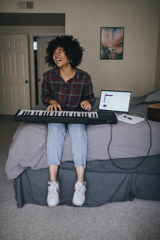 woman on bed using a midi controller keyboard with laptop